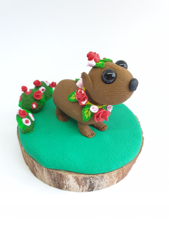 Rosie the wombat is a adorable sculpture with a crown and necklace of pink and red roses and green leaves.