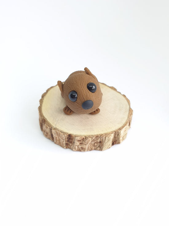 very cute brown baby wombat with black eyes sculpture. hand made from polymer clay on a round wooden base.