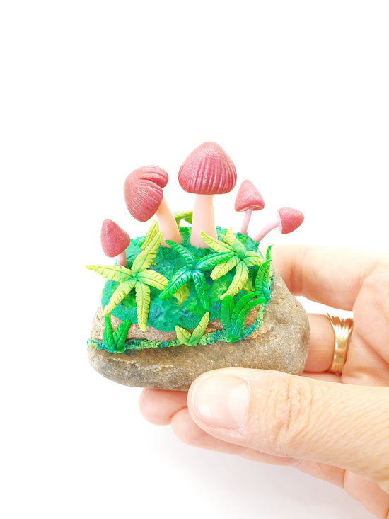 Pink shimmer mushrooms on rock surrounded by fern and moss, all  sculpted out of polymer clay