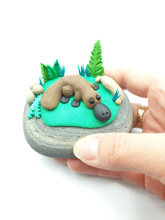 Polymer clay miniature platypus sculpture. Hand made with incredible detail. Adorable, cute Australian native platypus animal sculpture on a real rock surrounded by sculpted ferns and plants.
