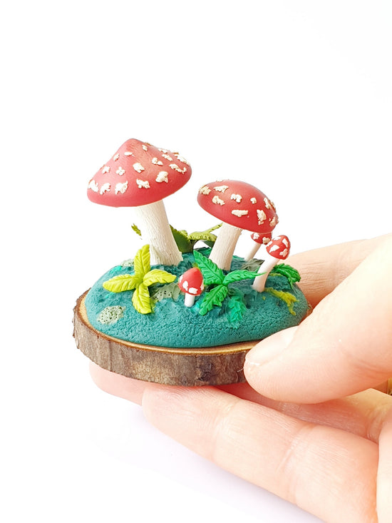 Miniature red and white amanita mushrooms, toadstools, fungi and ferns sculpture. Hand sculpted from polymer clay with a round wooden slice base.