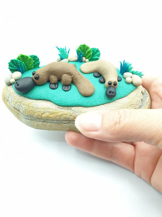 Polymer clay miniature platypus sculpture. Hand made with incredible detail. A pair of adorable, cute Australian native platypus animal sculpture on a real rock surrounded by sculpted ferns and plants.